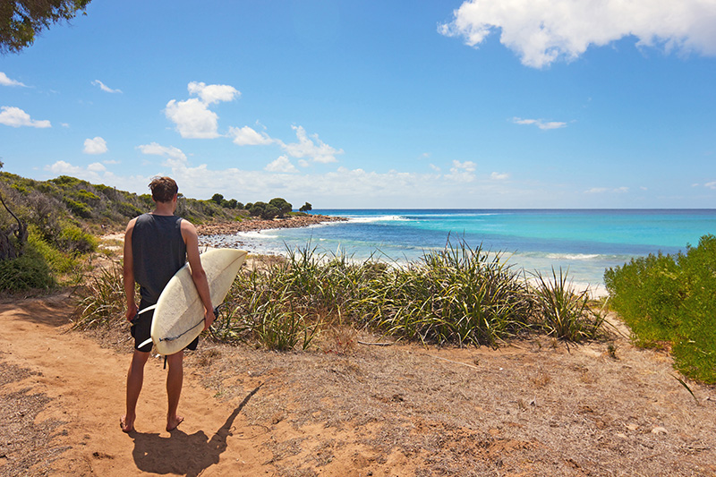 Surfer holding his surfboard on the beach in Margaret River, Western Australia