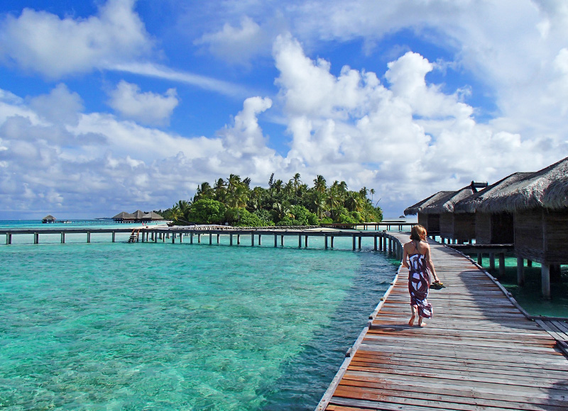 Eco-tourist walking on the boardwalk with crystal clear water in the Maldives